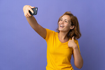 Young Georgian woman isolated on purple background making a selfie with mobile phone