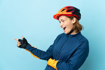 Young cyclist woman isolated on blue background pointing finger to the side and presenting a product