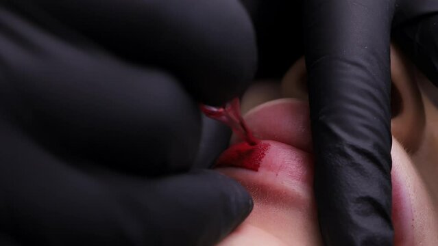 Macro shot as the tip of the tattoo machine introduces pigment to the lips of the girl model who is on the procedure. High quality 4k footage Generative AI