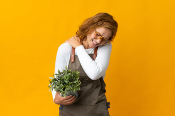 Young Georgian woman holding a plant isolated on yellow background suffering from pain in shoulder for having made an effort