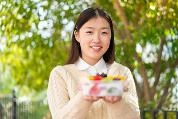 Youing chinese woman holding a bowl of fruit at outdoors