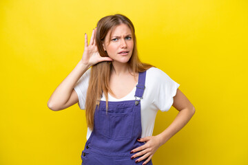 Young caucasian woman isolated on yellow background listening to something by putting hand on the ear