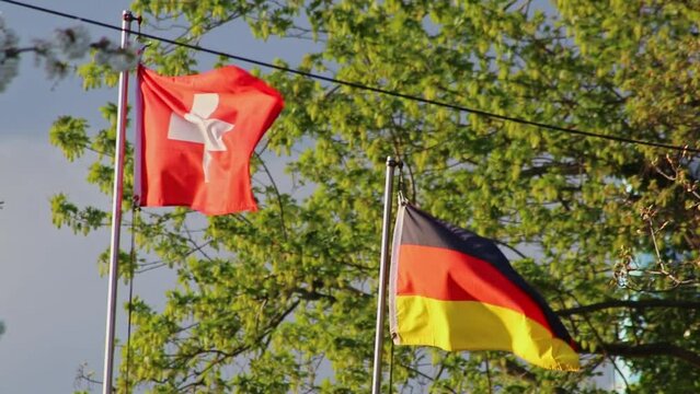 Swiss flag and german flag side to side show swiss german friendship and german swiss relations with fluttering flags on windy day as governmental cooperation and symbol for conflicts or agreement