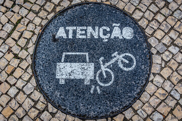 Warning sign on a manhole cover on a bicycle lane in Lisbon city, Portugal