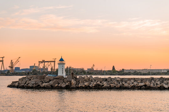 Sunset landscape with the Genoese lighthouse that has a blue roof, from the pier made of rocks, in a port on the Black Sea.