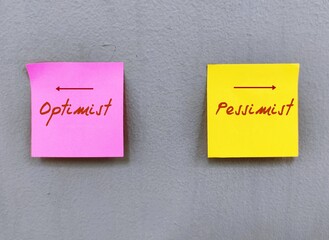 Pink and yellow stick note on wall with text and direction point to OPTIMIST and PESSIMIST in opposite way - concept of choose to be optimistic positive mindset or be pessimistic or negative thinking