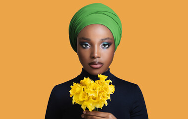 African beautiful girl in a colored headscarf on her head holding flowers in her hand.