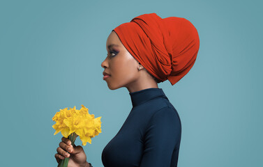 African beautiful girl in a colored headscarf on her head holding flowers in her hand.