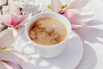 Milk dissolves in a mug of coffee. white cup with cappuccino with blooming magnolia branches on a white background. Good morning concept. Hot drinks with caffeine concept.
