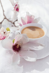 white cup with cappuccino with blooming magnolia branches on a white background. Spring still life composition. Good morning concept