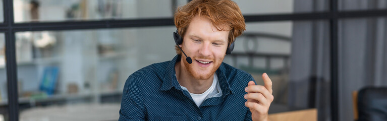 Smiling man call center worker in headphones is working at modern office. Portrait of a happy male support employee, smiles - obrazy, fototapety, plakaty