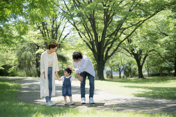 Obraz premium 公園をお散歩する仲良し家族 新緑の中手をつなぐファミリーのイメージ 広角 右にコピースペースあり