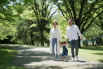 公園をお散歩する仲良し家族 新緑の中手をつなぐファミリーのイメージ...