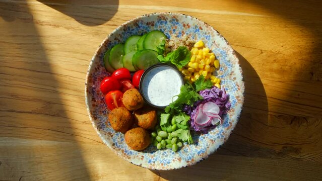Top view - Chickpea falafel salad with vegetables, quinoa and Edamame beans with Zaziki sauce on a wooden table. Healthy vegetarian food. High quality 4k footage. Bright, juicy fresh rations. Healthy