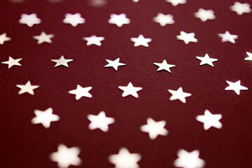 Red abstract holiday background or texture with silver stars confetti on  background. Copy space. Good backdrop for Christmas and New Year cards.