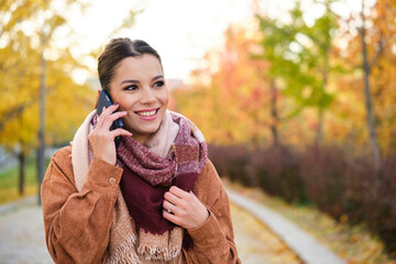 Caucasian young woman on a phone call smiling in autumn.