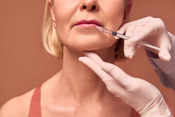 Cropped image of adult woman on beige background. Hands in white gloves and a medical gown make a...