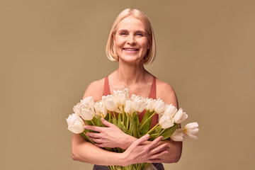 Women's beauty and spring.Portrait of a beautiful middle-aged woman holding a bouquet of white tulips and smiling on an olive background.