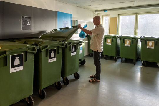 Stockholm, Sweden A man throws garbage in a super clean and organised garbage room in a residential housing complex.The labels denote type of waste in Swedish.