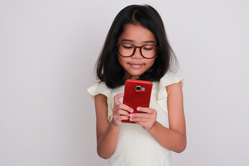 Asian kid smiling while looking to mobile phone that she hold