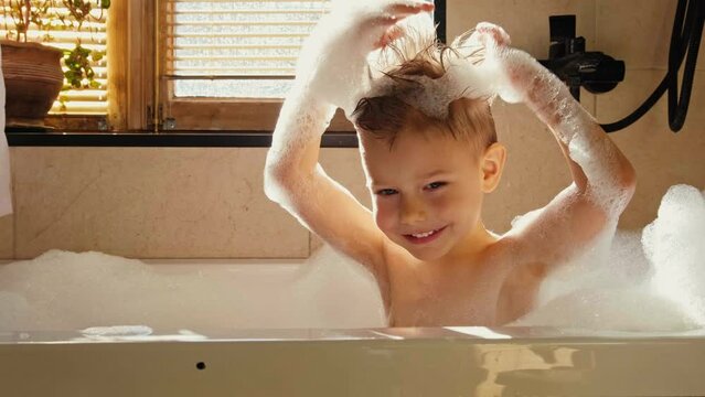 A little boy bathes in a bath. Bath games. Daily care. Shampoo and bath foam. The child bathes. Boy playing with dinosaurs.