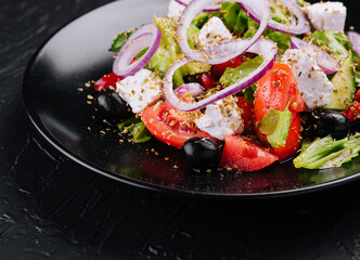 Greek salad in black bowl on stone