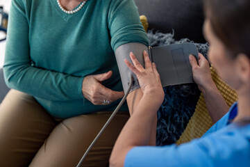 Unrecognizable senior woman visited by home care specialist getting her blood pressure measured. Nurse teaching elderly woman to measure blood pressure at home. Home care for people in retirement.