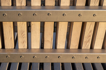 Wooden bars are fixed with screws on an iron profile. Wooden bars are vertically screwed to horizontal profiles. The sun illuminates the fence made of wooden bars.