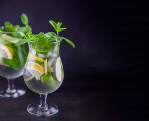 Summer mint lime refreshing cocktail mojito with ice in glass on black background copy space. Carbonated mineral water and lemon. Glass for drinks. Lemonade at the bar menu. Classic sparkle drink.