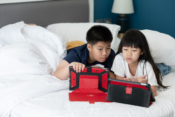 two chinese children addicted tablet, asian child watching telephone together on their bed, kid using smartphone