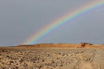 Rainbow in a sky over rocky desert and distant mountains in the wild. Wonderful world. Environment protection