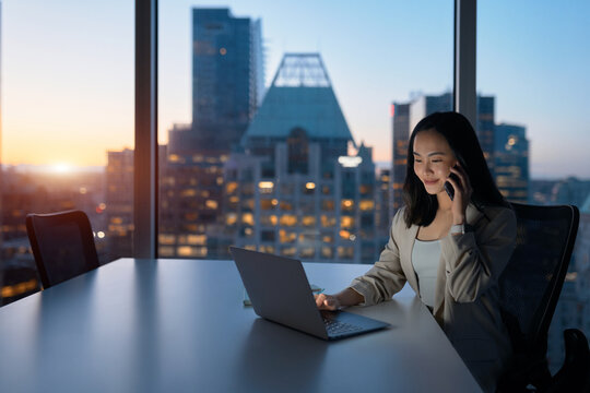 Young busy Asian business woman executive working on laptop making call at night in dark corporate office. Professional businesswoman manager talking to client using computer, city Generative AI