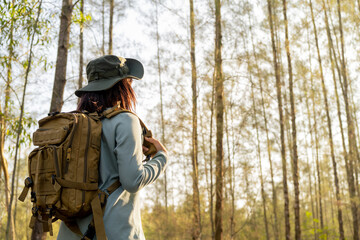 Obraz premium Young Asian girl with a backpack and hat hiking in the mountains during the summer season, a traveler walking in the forest. Travel, adventure, and journey concept.