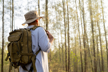 Young Asian man with a backpack and hat hiking in the mountains during the summer season, a traveler walking in the forest. Travel, adventure, and journey concept.