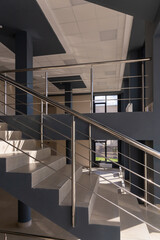 Stairs in a concrete office building in neutral tones, covered with ceramic tiles, with shiny metal railings