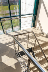 Obraz premium Stairs in a concrete office building in neutral tones, covered with ceramic tiles, with shiny metal railings