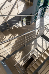 Stairs in a concrete office building in neutral tones, covered with ceramic tiles, with shiny metal railings