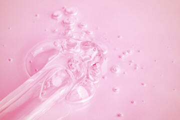 A flowing clear gel from a pipette. A lot of flowing gel in a big drop. With bubbles. On a pink background.
