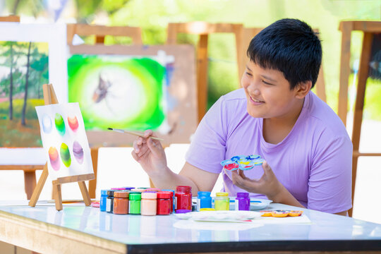 happy teenage boy compare of primary colors while painting watercolor outdoors, concept of teens activites, hobby,talent and drawing makes teens express their feelings and spark their creativity