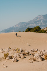 Lonely woman on dunes with a white dog Patara Beach Turkey.