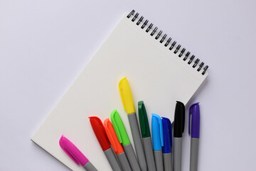 A blank notepad and coloured felt-tip pens on a white background. Multicoloured felt-tip pens for children's drawing. Flat plan, top view, space for copying.