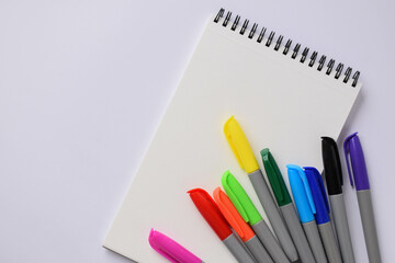 A blank notepad and coloured felt-tip pens on a white background. Multicoloured felt-tip pens for children's drawing. Flat plan, top view, space for copying.