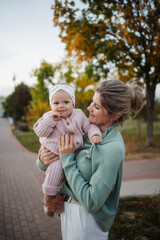 Fototapeta na wymiar Mom smiling, holding and hugging her happy daughter infant on the street in the park in the fall. Communication harmonious development. Autumn leaves. Infant care, day, mothers, parenthood, maternity