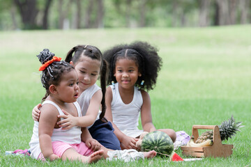 Little African and Caucasian kids picnic and playing in the park. Little cute girl hugging and...