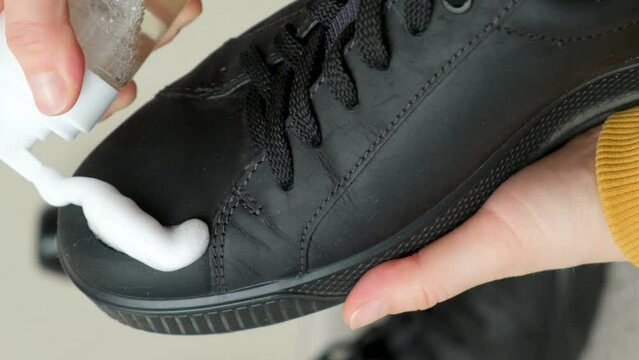 Applying cleaning foam from a bottle to nubuck men's shoes
