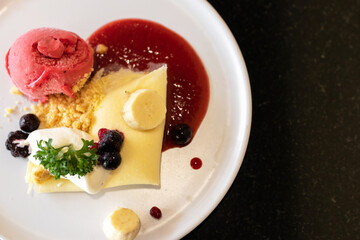 Soft crape with sorbet ice cream with berry juicy sauce and banana sliced with crumble.