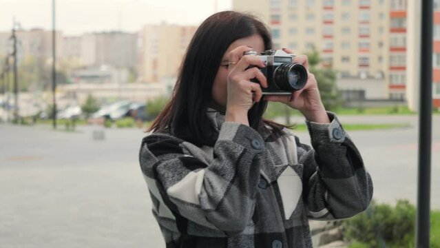 Attractive and pleasant young woman taking pictures with old vintage film camera in a city street