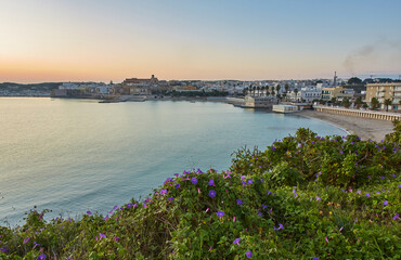 beautiful orange sunset or sunrise over the harbor of Otranto, Italy. Soft clouds, calm ocean and backlit skyline and marina with yachts and fishermen.