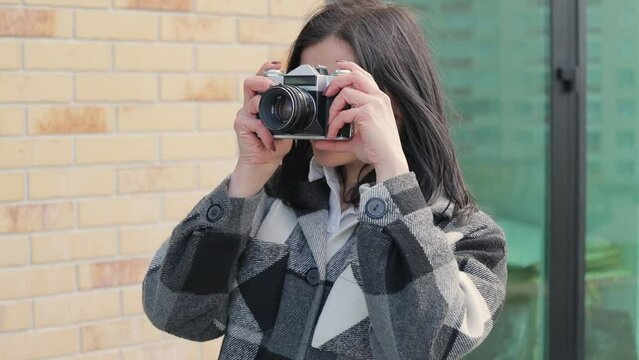Attractive and pleasant young woman taking pictures with old vintage film camera in a city street, slow motion