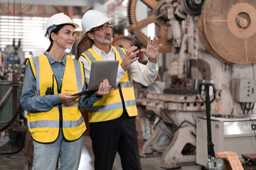 Senior manager train female technician to work in metalwork production factory. Industrial engineer man and woman standing in manufacturing facility talking machinery technology in heavy industry.